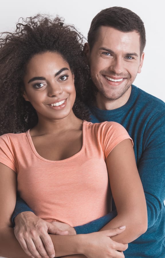 Man holding woman from behind while they both smile