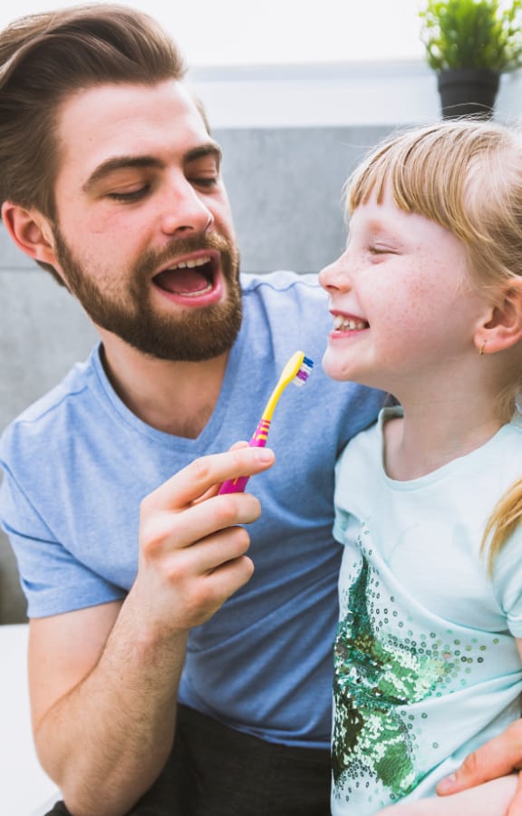 Father brushing his daughters teeth