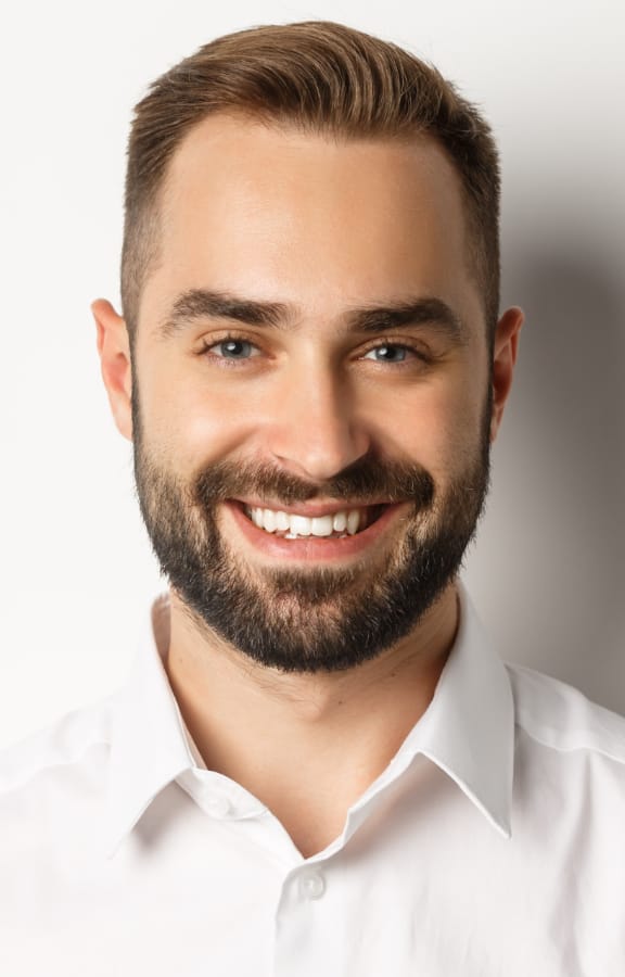Middle aged man smiling and standing in front of a white wall